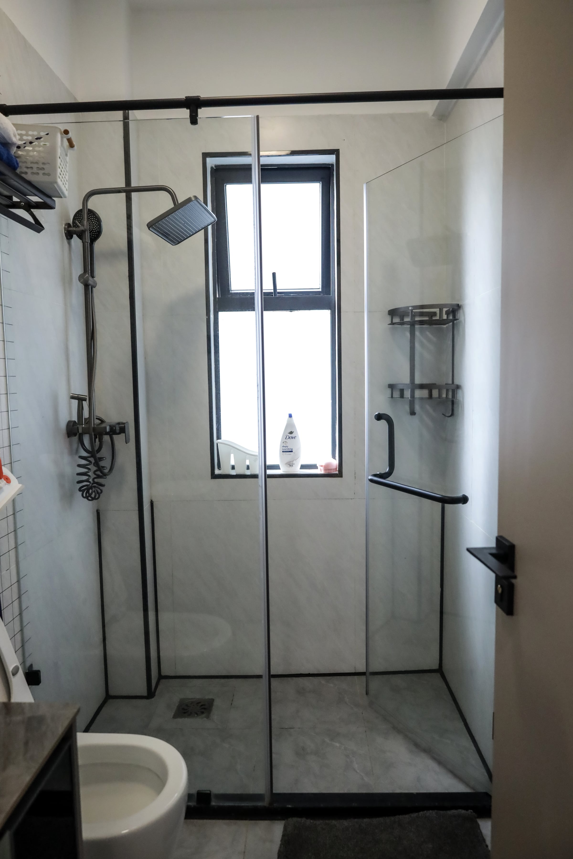Walk-in rainfall shower behind clear glass, lit by a tall window
